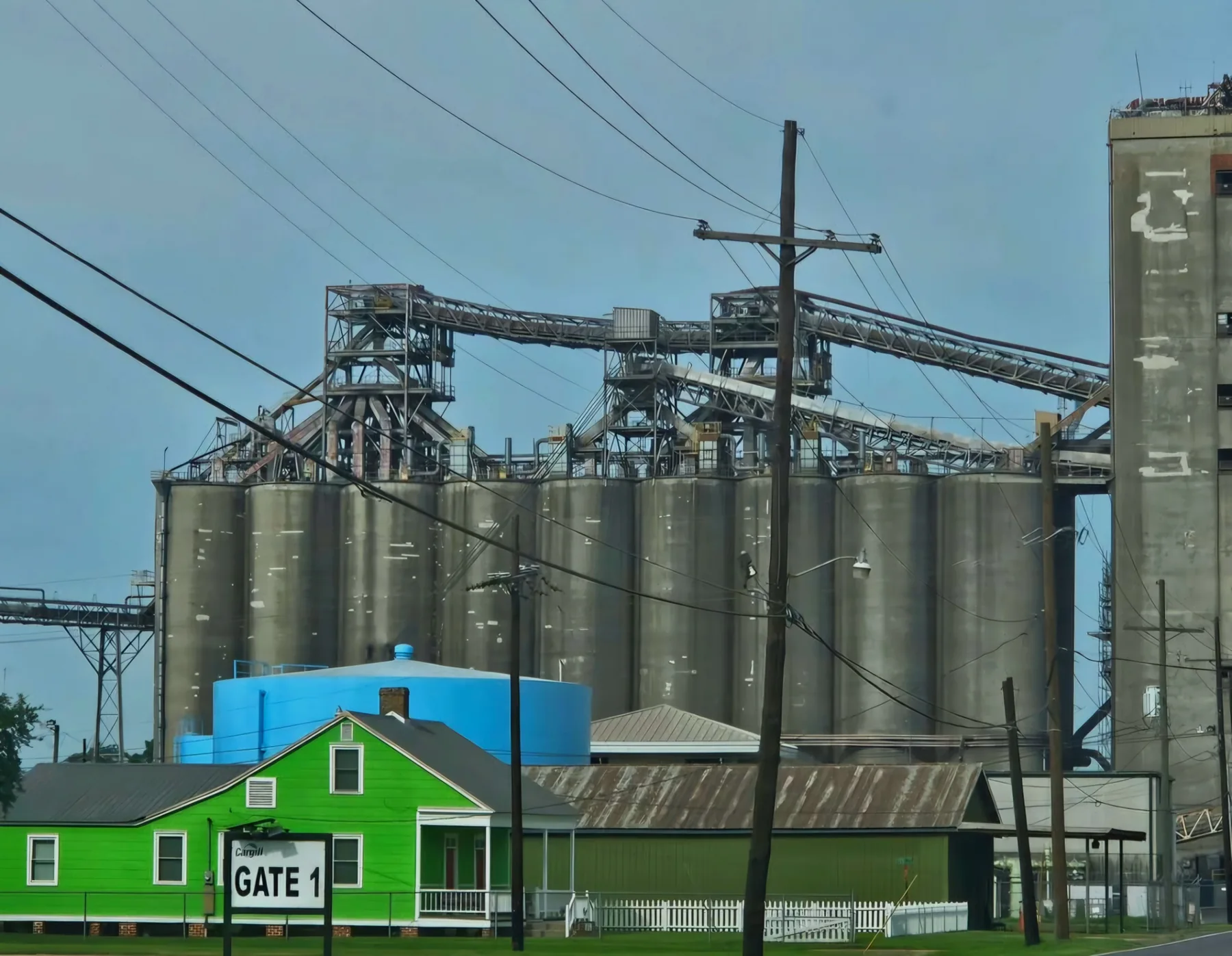 Une maison verte devant des silos industriels
