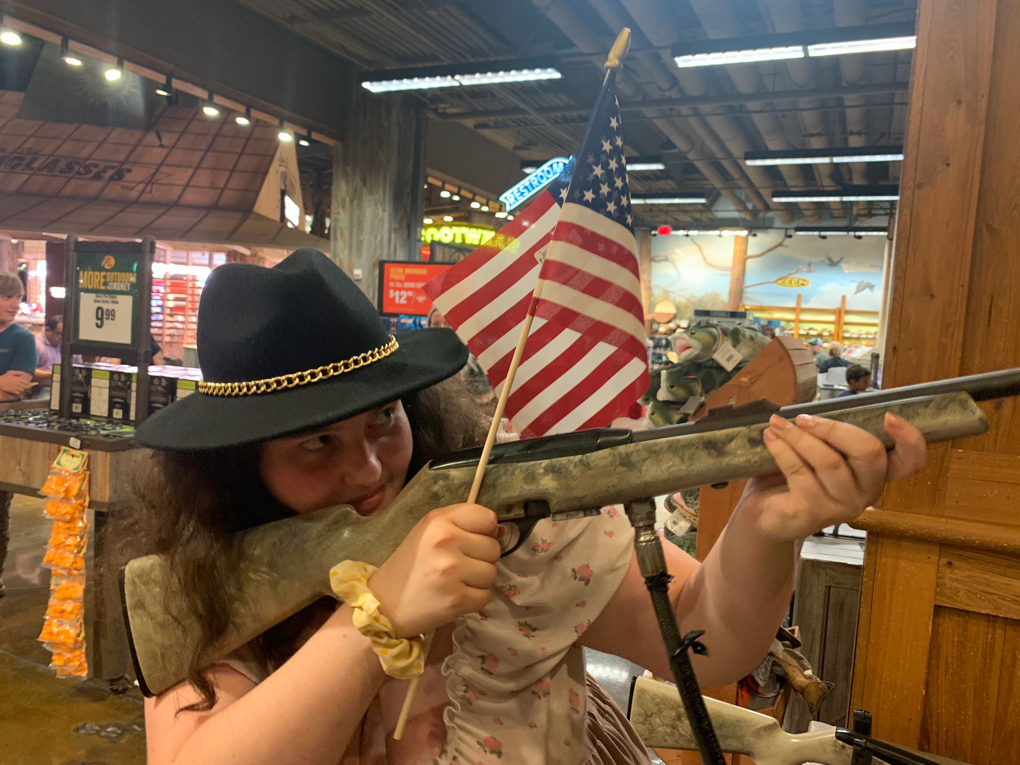 J'ai un chapeau et je tiens une carabine, un drapeau USA et je suis dans un magasin de chasse et de pêche