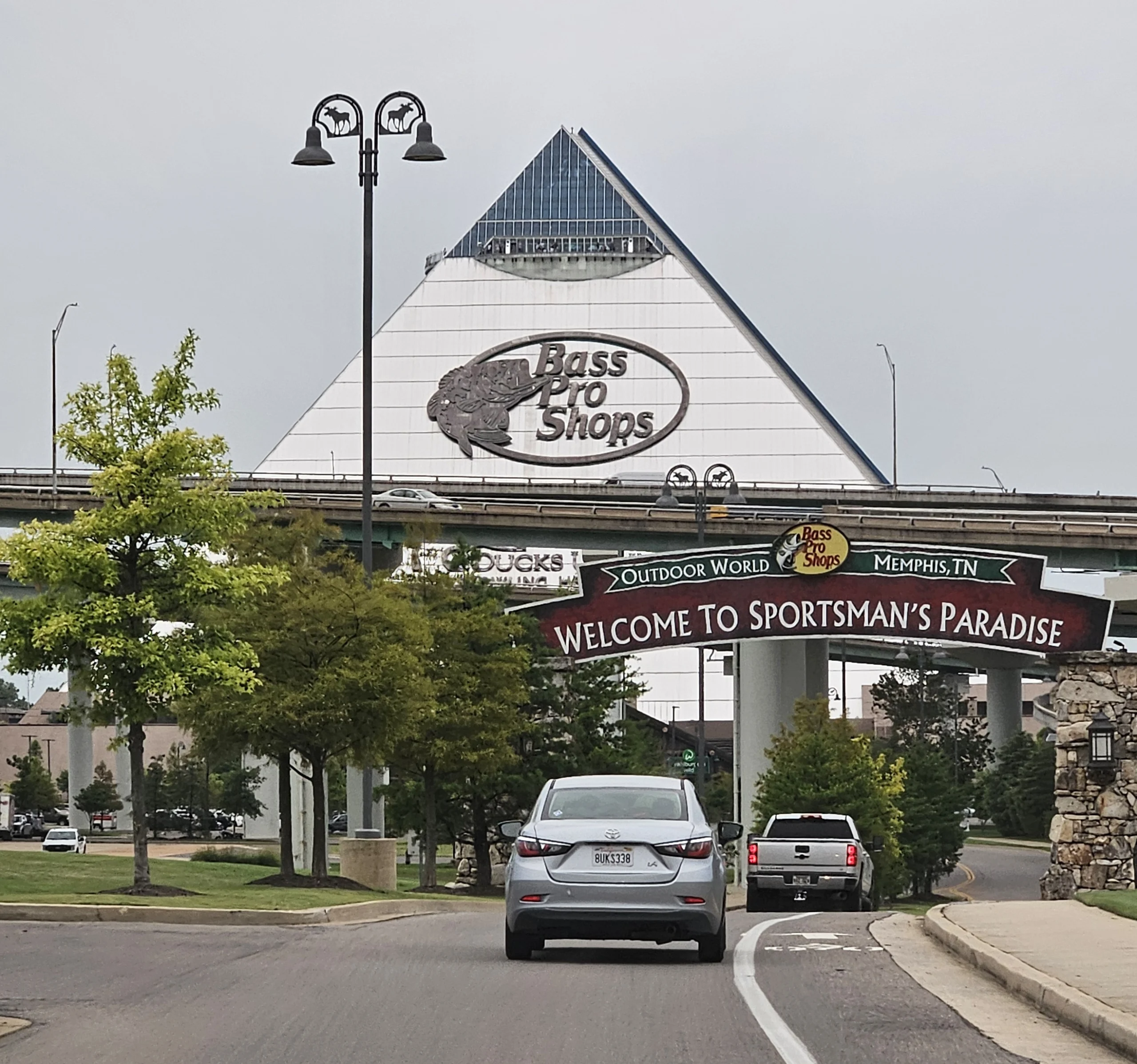 Des voitures qui vont vers une géantes pyramide blanche qui dit bass pro shop et un panneau welcome