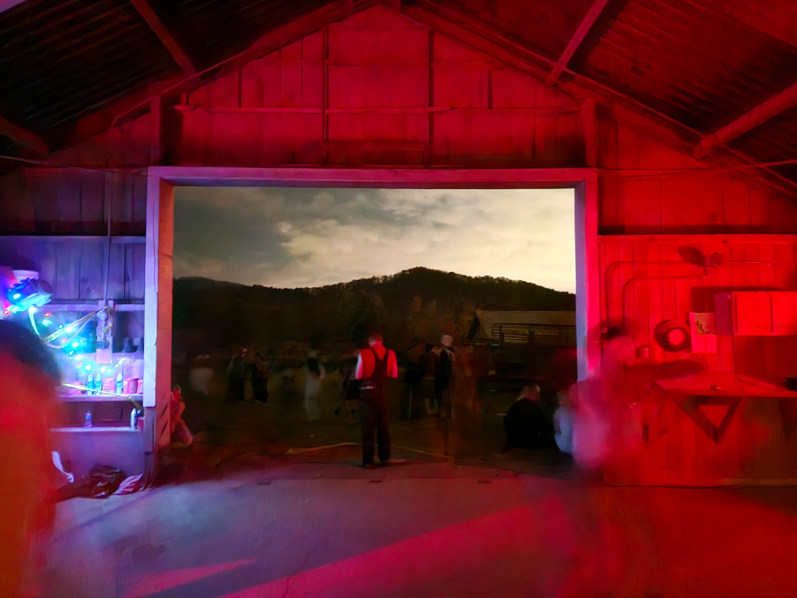 Une grange avec de la lumière rouge, des gens flous, et dans l'ouverture des montagnes